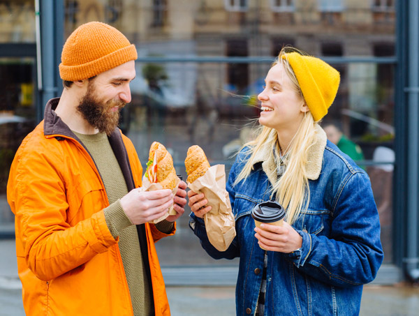 two friends sharing food and drinks outdoors in casual attire with pastries and coffee